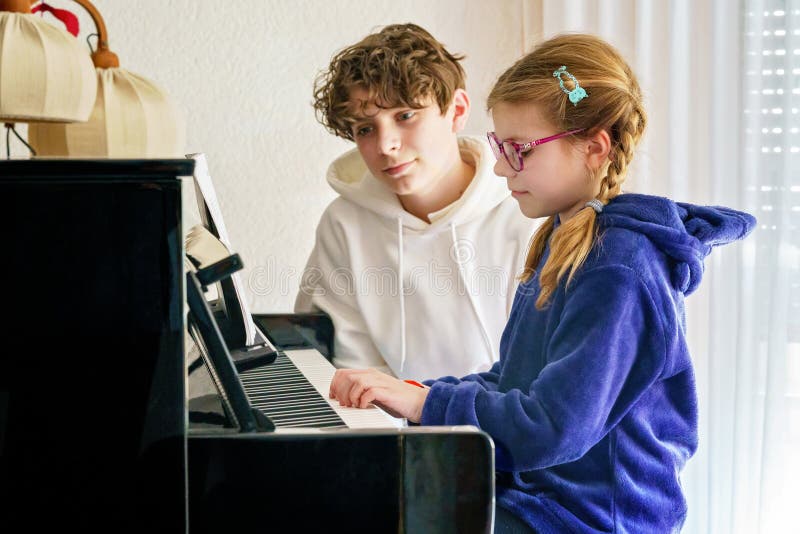 Ungefär skolflicka som utövar piano medan en tonårspojke lyssnar uppmärksamt. Barndom i musikinlärning fotografering för bildbyråer