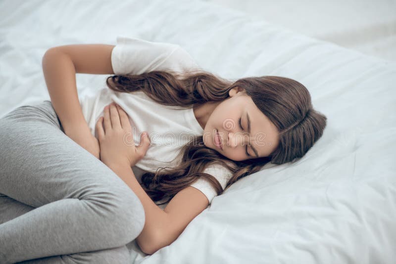 Unglückliche Jugendliche, die Bauch mit den Händen halten liegt lizenzfreie stockfotos