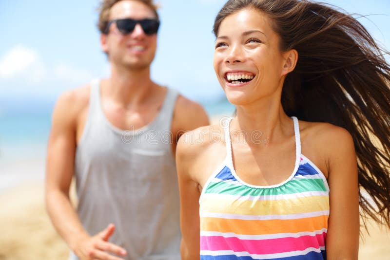 Young happy couple laughing having fun on beach. couple holding hands running playful and cheerful smiling happy on beach outside during summer vacation. Asian woman, Caucasian man. Young happy couple laughing having fun on beach. couple holding hands running playful and cheerful smiling happy on beach outside during summer vacation. Asian woman, Caucasian man.