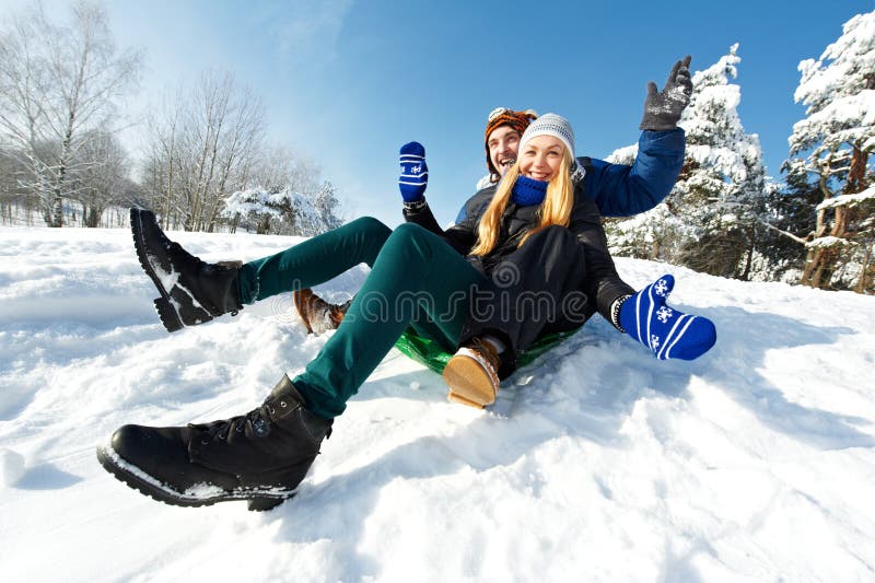 Happy young smiling adult people in warm clothing sledding on snow at winter outdoors. Happy young smiling adult people in warm clothing sledding on snow at winter outdoors