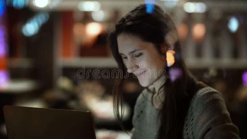 Ungt lyckligt kvinnasammanträde på kafét och använda bärbara datorn Beskåda inom fönstret på kvinnlign som surfar internet