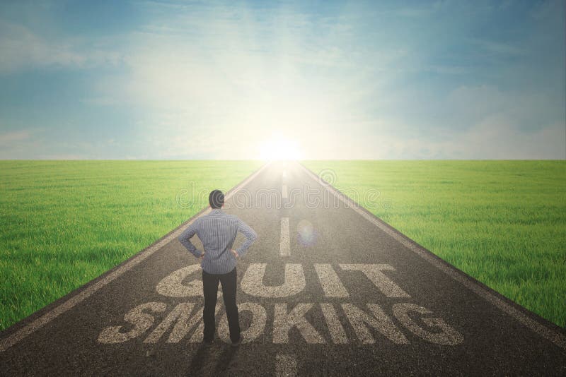 Back view of young male standing on a text of quit smoking while looking at the sunbeam on the end road. Back view of young male standing on a text of quit smoking while looking at the sunbeam on the end road