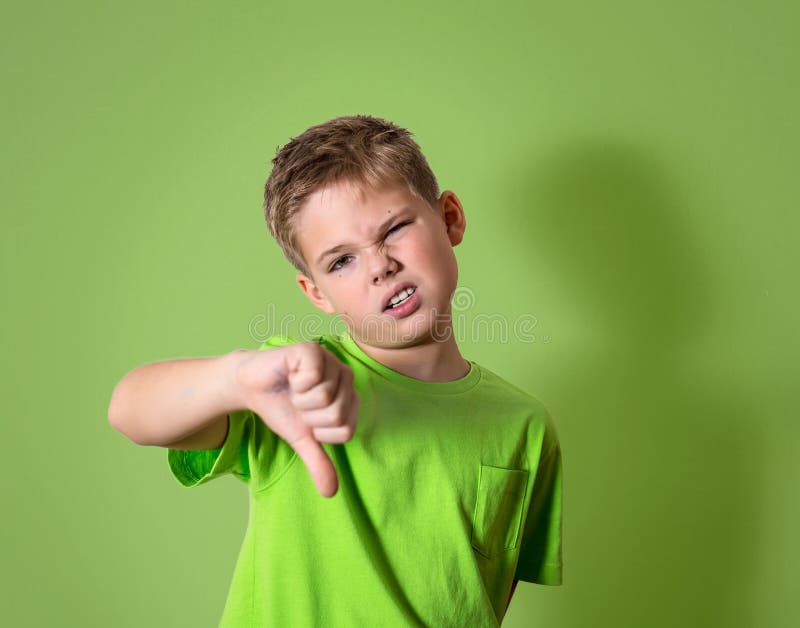 Portrait unhappy, angry, displeased child giving thumbs down hand gesture, isolated on green background. Negative human face expressions, emotions, feelings, attitude, life perception, body language.