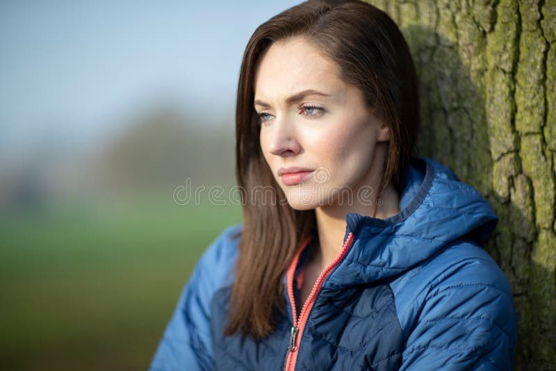 Unhappy Looking Young Woman Leaning Against Tree On Winter Walk In Park