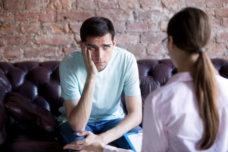 Unhappy male patient listening to a psychologist counselor. stock photo