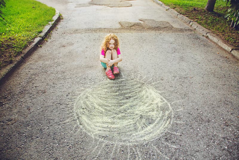 Unhappy, poor child sitting on asphalt with drawing sun. Unhappy, poor child sitting on asphalt with drawing sun.