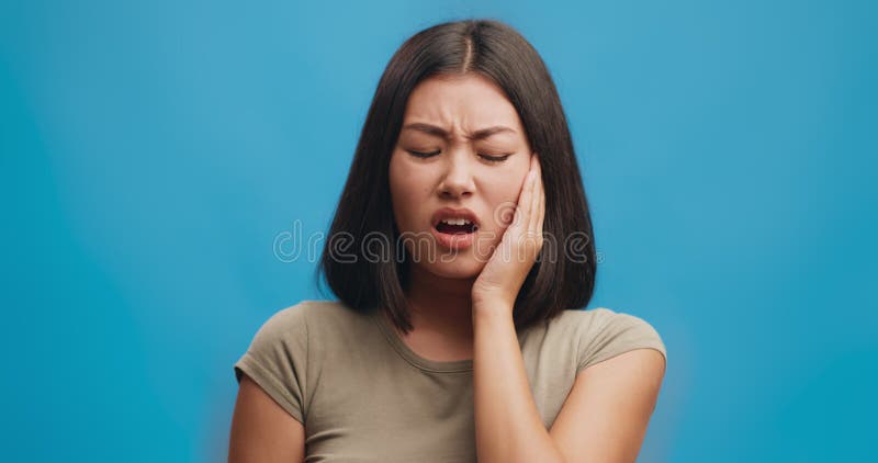 Unhappy young asian woman touching cheek, suffering from toothache, having terrible sudden tooth pain