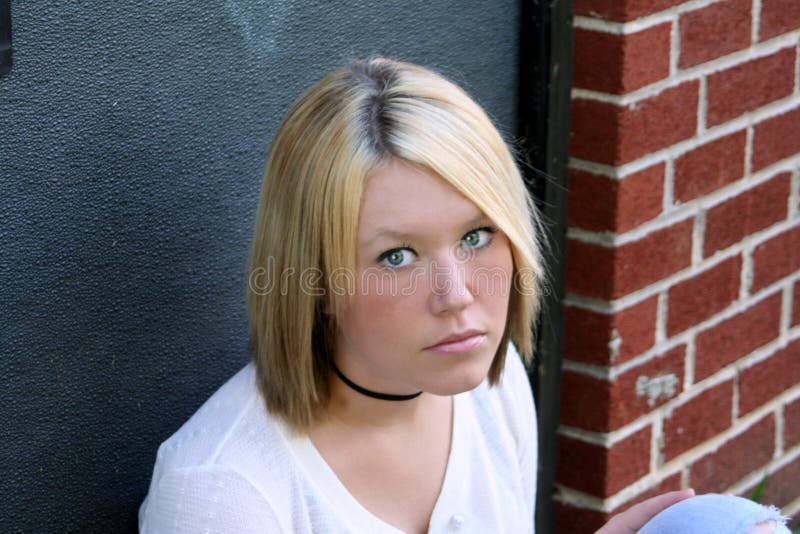 Unhappy young blond woman, sitting near an exterior doorway of a building. Unhappy young blond woman, sitting near an exterior doorway of a building.