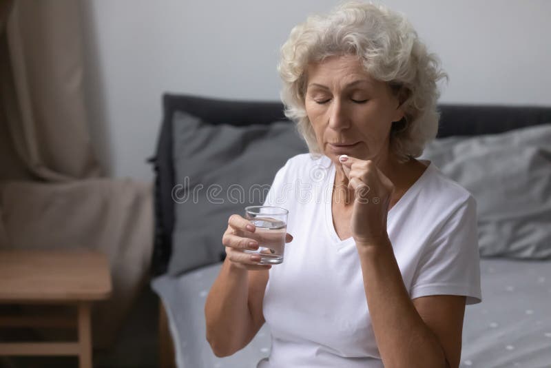 Unhealthy senior woman holding glass of water taking daily pill