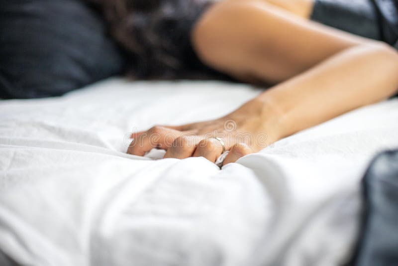 An Unidentifiable Married Woman Lies in Bed Wearing a Silk Nightgown while Her Hand Grabs on To the Bed Sheets, Sensuality Concept Stock Photo picture