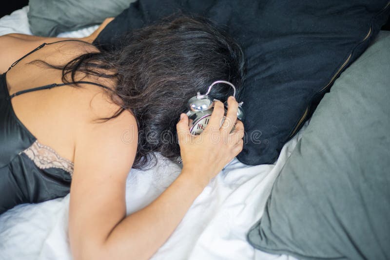 An unidentifiable woman wearing a silk nightgown lies in bed while grabbing the alarm clock royalty free stock photos An unidentifiable woman wearing a silk nightgown lies in bed while grabbing the alarm clock royalty free stock photos