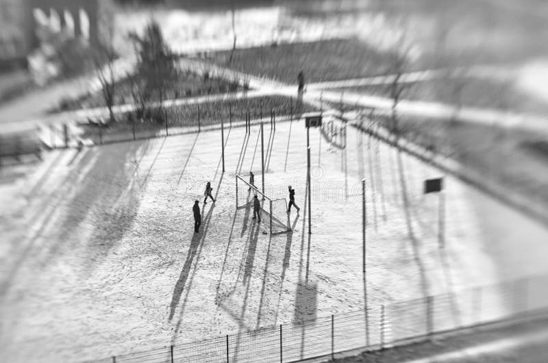 Unidentified children and an adult in the distance play soccer tilt shift effect in the black and white style