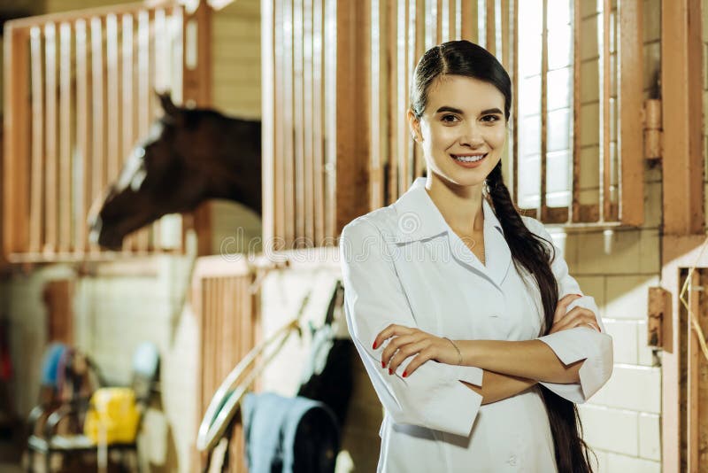 Uniforme branco vestindo da mulher de olhos escuros que está no estábulo imagens de stock Uniforme branco vestindo da mulher de olhos escuros que está no estábulo imagens de stock