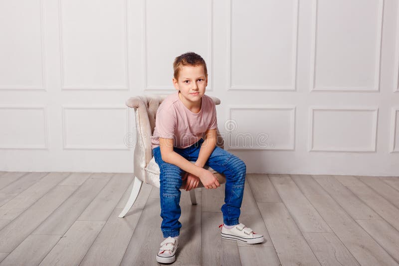 Uninhibited European boy in white sneakers and jeans sits in a chair