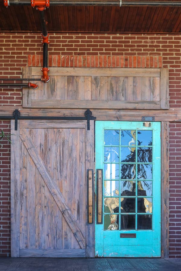 Unique rustic barn door entrance to building with reflection of nature in one side with glass panes all set in brick with red