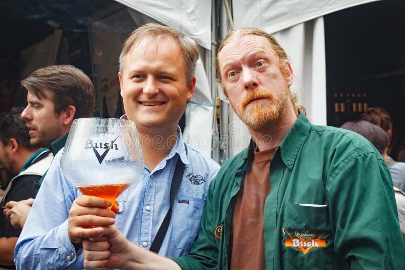 BRUSSELS, BELGIUM - SEPTEMBER 07, 2014: Unknown men with the big glass of the amber Bush beer. royalty free stock photos BRUSSELS, BELGIUM - SEPTEMBER 07, 2014: Unknown men with the big glass of the amber Bush beer. royalty free stock photos