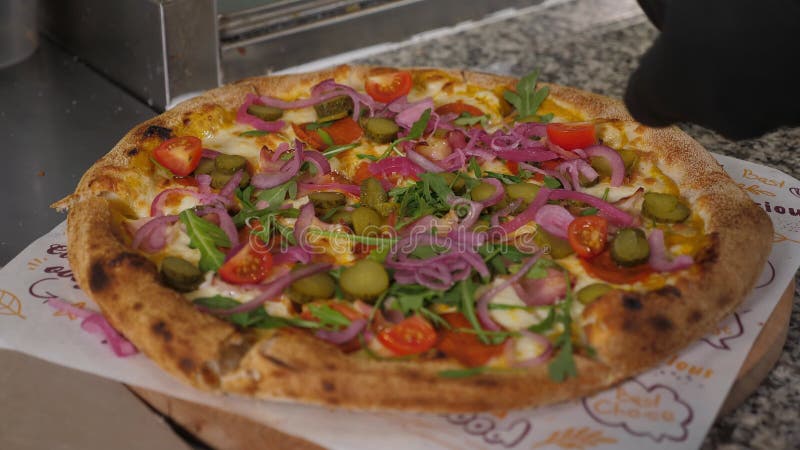 Uno chef che decora una pizza appena cotta con sottaceti di cipolla rossa e rucola.