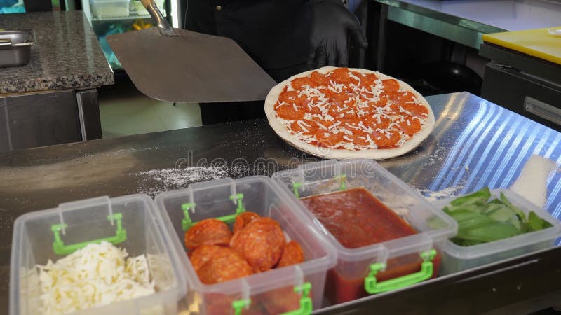 Uno chef in uniforme e guanti mette la pizza su una speciale spatola in cucina. archivi video