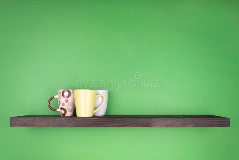 Uno scaffale di colore scuro con la strutturazione del legno è installato su una parete verde; sullo scaffale ci sono tre tazze i immagine stock libera da diritti Uno scaffale di colore scuro con la strutturazione del legno è installato su una parete verde; sullo scaffale ci sono tre tazze i immagine stock libera da diritti