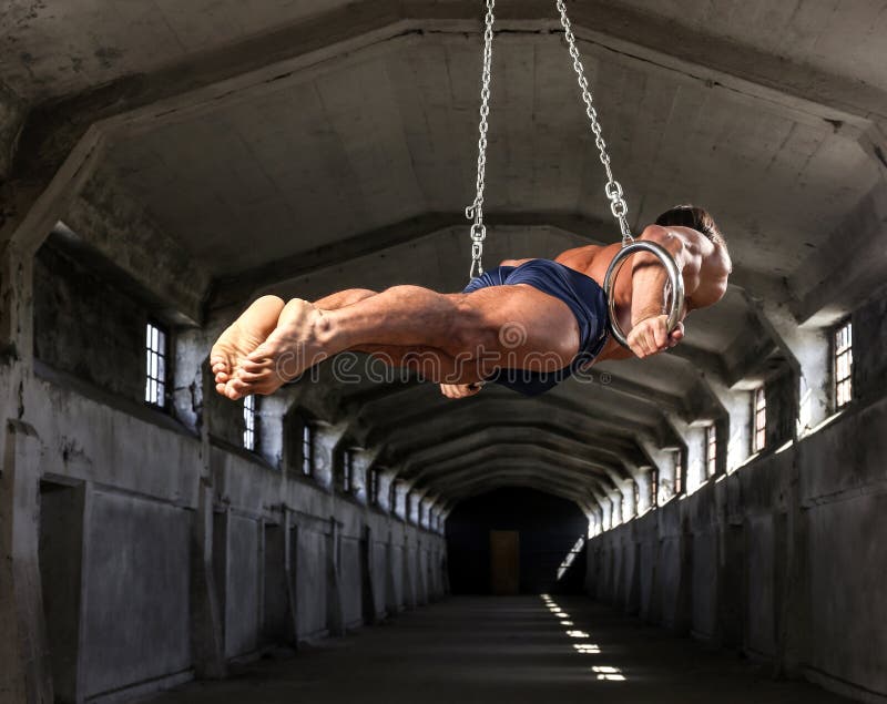Uno sportivo professionista con treni i bei di un corpo muscolare sugli anelli relativi alla ginnastica in fabbricato industriale fotografia stock libera da diritti Uno sportivo professionista con treni i bei di un corpo muscolare sugli anelli relativi alla ginnastica in fabbricato industriale fotografia stock libera da diritti