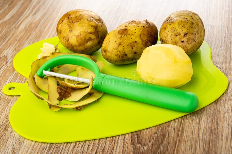 Unpeeled peeler картофеля слез картофель и апельсина на разделочной доске на столе стоковое изображение rf