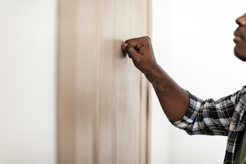 Unrecognizable African American Guy Knocking Standing Near Door Indoors, Cropped