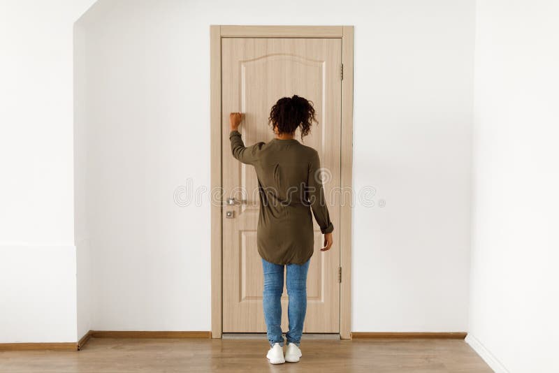 Unrecognizable African American Woman Knocking At Door Indoors, Rear View