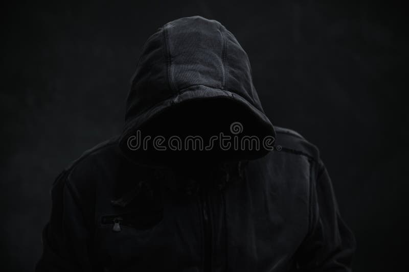 Unrecognizable cyber criminal or computer hacker wearing black hooded jacket, low key portrait stock images