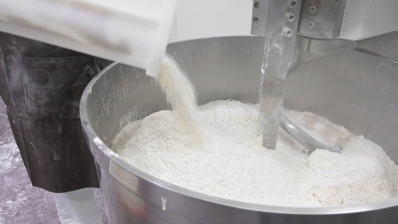 Unrecognizable person pouring the flour at the electric mixer at bakery kitchen, mixing the dough