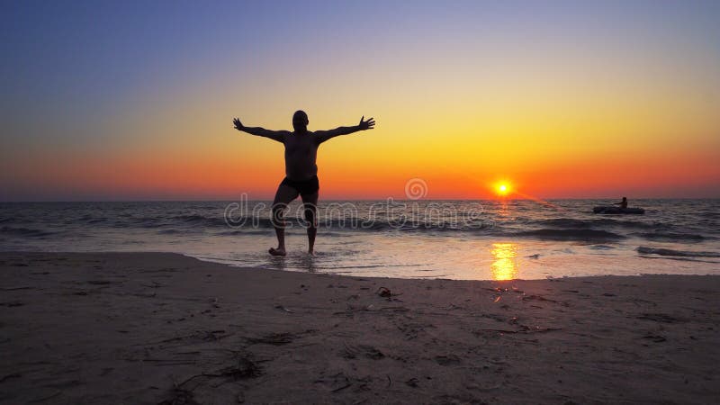 Unrecognizable silhouette walk out of ocean sunset water with hands wide open royalty free stock photography