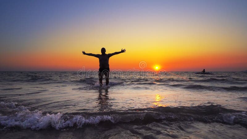Unrecognizable silhouette walk out of ocean sunset water with hands wide open stock photo