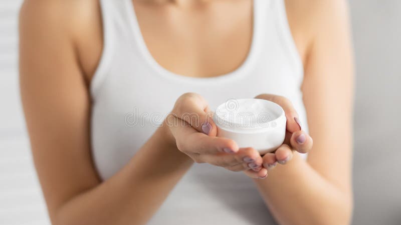 Unrecognizable Woman Holding Face Cream Jar, Gray Background, Cropped royalty free stock photo Unrecognizable Woman Holding Face Cream Jar, Gray Background, Cropped royalty free stock photo