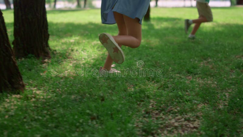 Unrecognized kid legs run on green lawn. Happy children play on fresh grass.