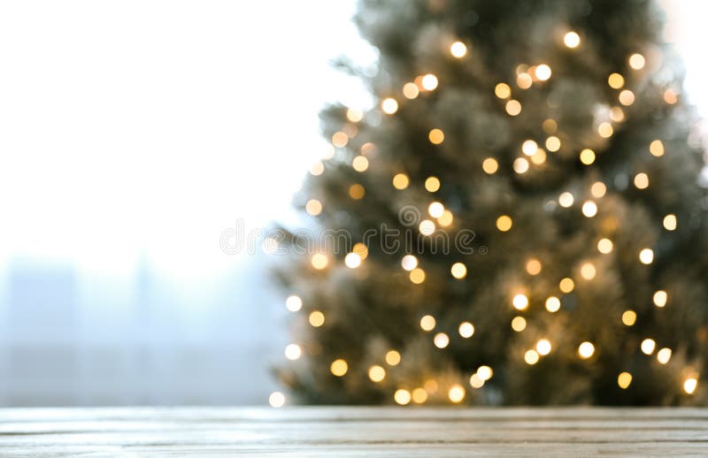 Unscharfe Aussicht auf den schönen Weihnachtsbaum mit Lichtern in der Nähe von Fenstern, Schwerpunkt auf Holztisch Textbereich stockbild