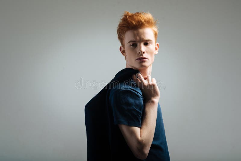 Unsmiling red-haired young man looking over his shoulder