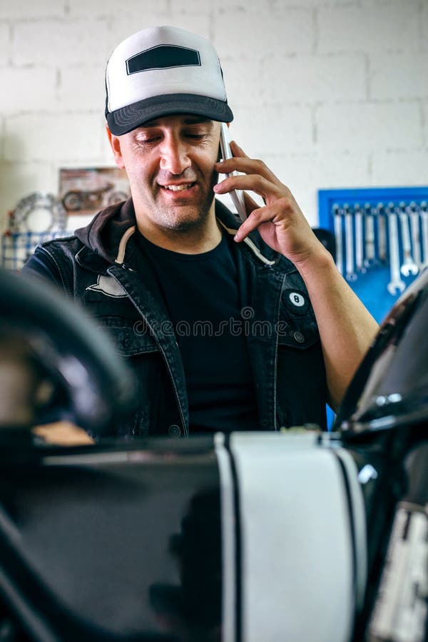 Unterhaltungstelefon des Mechanikers beim Reparieren des Motorrads stockfotos Unterhaltungstelefon des Mechanikers beim Reparieren des Motorrads stockfotos