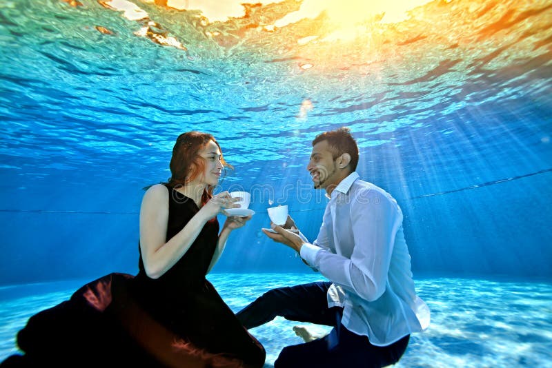 An unusual loving couple, a guy and a girl, look at each other, sitting underwater at the bottom of the pool with white stock photography An unusual loving couple, a guy and a girl, look at each other, sitting underwater at the bottom of the pool with white stock photography