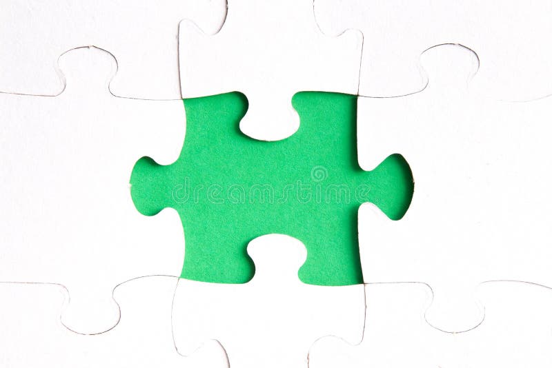 Unfinished puzzle made of white cardboard on a green background and one unsuitable part from another puzzle, one piece is missing, copy space. Unfinished puzzle made of white cardboard on a green background and one unsuitable part from another puzzle, one piece is missing, copy space
