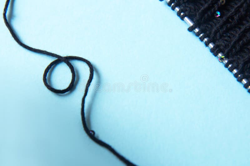 Unwound thread. Knitting black yarn and a ball of thread and knitting needles on blue background. Woman knitting woolen clothes