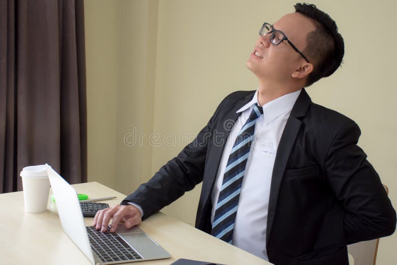 Uomini d'affari asiatici in un vestito che lavora duro e che ritiene doloroso toccando parte posteriore con expressionat fatto so fotografie stock Uomini d'affari asiatici in un vestito che lavora duro e che ritiene doloroso toccando parte posteriore con expressionat fatto so fotografie stock