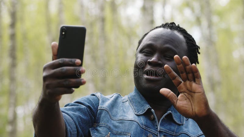 African man taking selfies or having videocall on his smartphone in the nature. High quality photo. African man taking selfies or having videocall on his smartphone in the nature. High quality photo