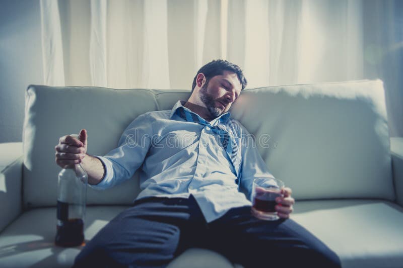 Uomo alcolico di affari nel sonno sciolto blu del legame potabile con la bottiglia di whiskey sullo strato immagini stock Uomo alcolico di affari nel sonno sciolto blu del legame potabile con la bottiglia di whiskey sullo strato immagini stock