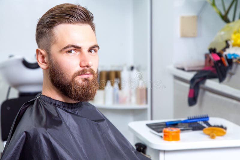 Uomo alla moda in un negozio di barbiere che esamina macchina fotografica fotografia stock Uomo alla moda in un negozio di barbiere che esamina macchina fotografica fotografia stock