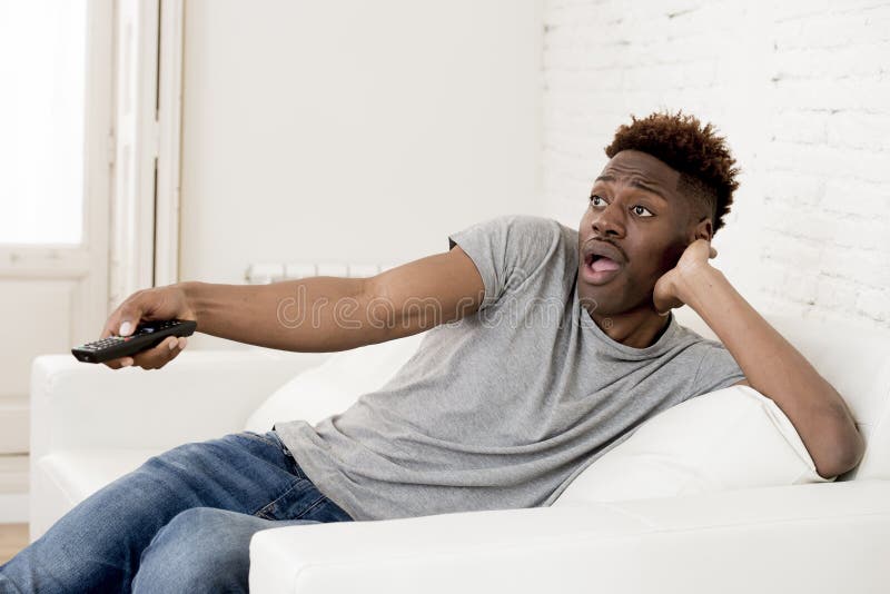 Uomo americano dell'africano nero attraente che si siede a casa la televisione di sorveglianza dello strato del sofà immagini stock Uomo americano dell'africano nero attraente che si siede a casa la televisione di sorveglianza dello strato del sofà immagini stock