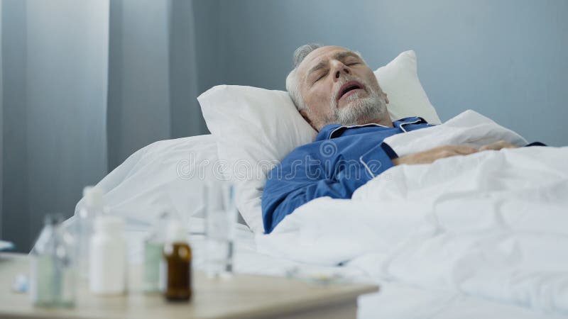 Uomo anziano che dorme a letto al reparto di ospedale, antibiotici che stanno sulla tavola fotografie stock libere da diritti Uomo anziano che dorme a letto al reparto di ospedale, antibiotici che stanno sulla tavola fotografie stock libere da diritti