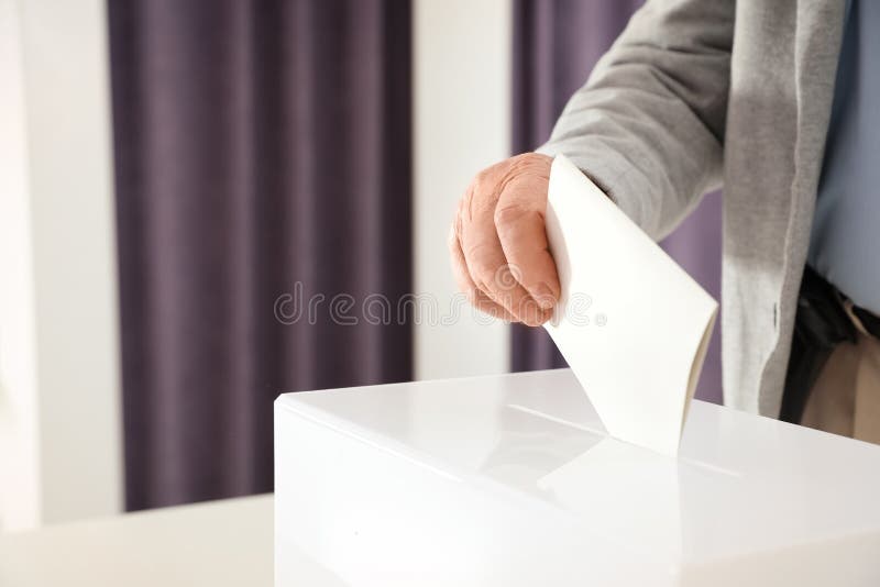 Uomo anziano che immette scheda elettorale nella scatola al seggio elettorale immagini stock libere da diritti Uomo anziano che immette scheda elettorale nella scatola al seggio elettorale immagini stock libere da diritti