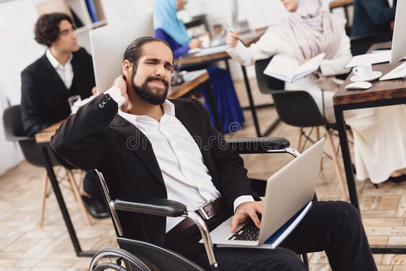 Uomo arabo disabile in sedia a rotelle che funziona nell'ufficio Ferite del collo del ` s dell'uomo fotografia stock Uomo arabo disabile in sedia a rotelle che funziona nell'ufficio Ferite del collo del ` s dell'uomo fotografia stock