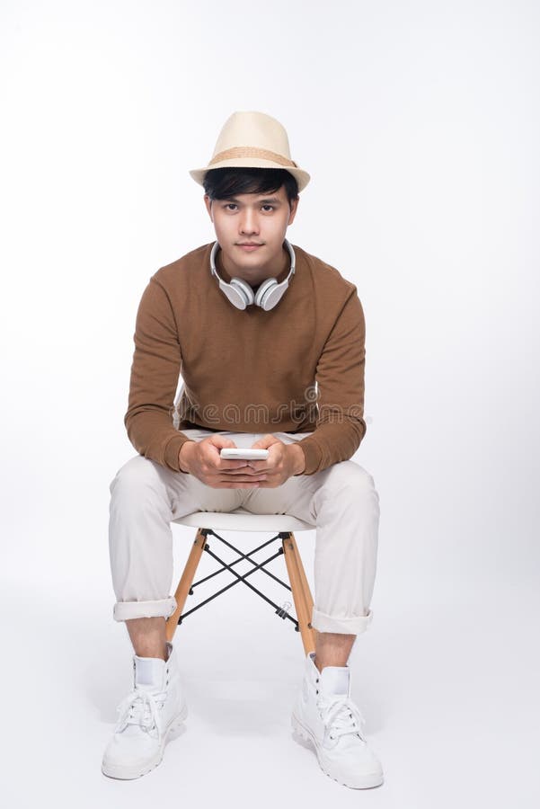 Uomo asiatico casuale astuto messo sulla sedia, tenente smartphone in st fotografia stock libera da diritti Uomo asiatico casuale astuto messo sulla sedia, tenente smartphone in st fotografia stock libera da diritti