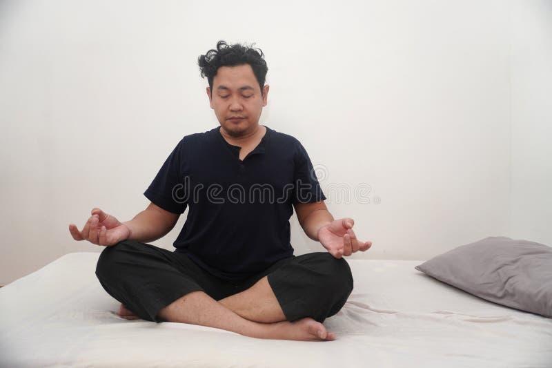 Uomo asiatico che fa yoga nella sua stanza da letto allungando e facendo esercizio di meditazione dopo essersi svegliato al mattin fotografia stock