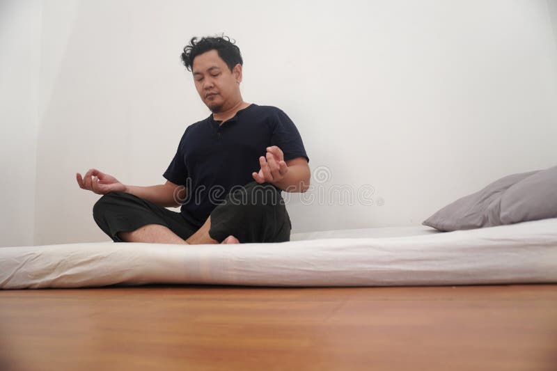 Uomo asiatico che fa yoga nella sua stanza da letto allungando e facendo esercizio di meditazione dopo essersi svegliato al mattin fotografia stock libera da diritti
